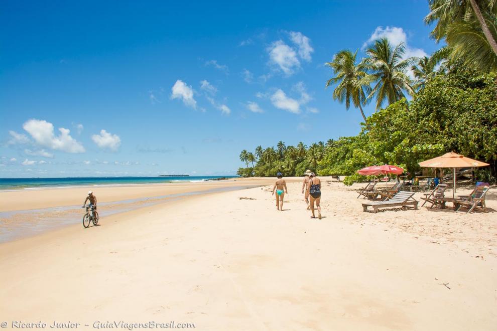 Imagem três senhoras caminhando e um rapaz andando de bicilceta na bela praia.